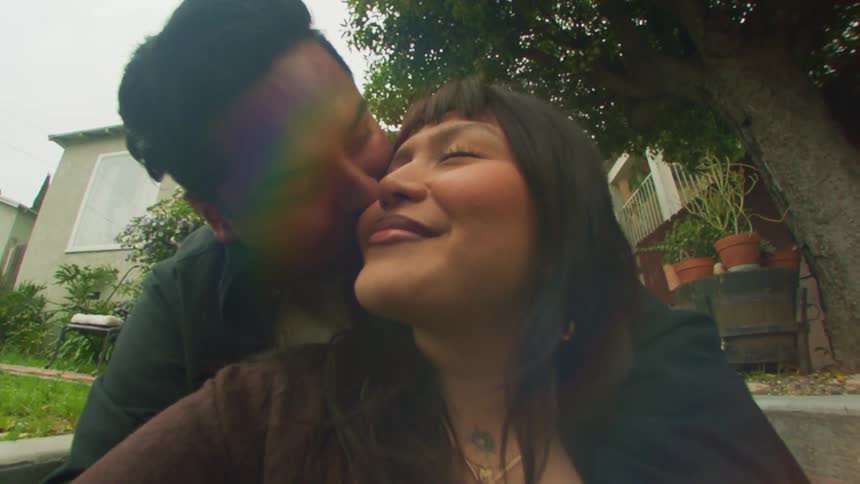 Portrait of man giving his girlfriend a kiss on the cheek while sitting on a staircase in an outdoor setting