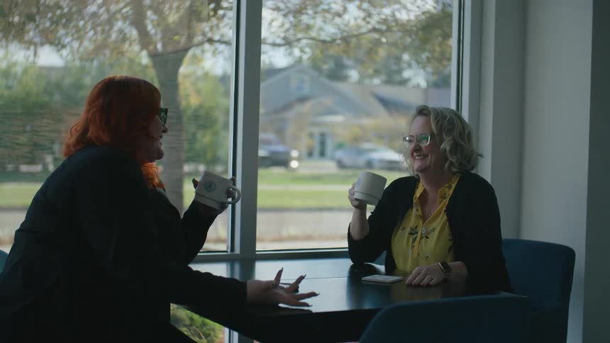 Two women sitting at a table drinking coffee talking