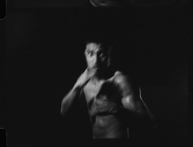 Black and white footage of a young shirtless man boxing