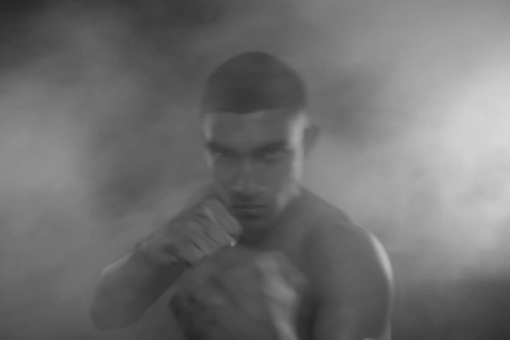 A young shirtless boxer surrounded by smoke