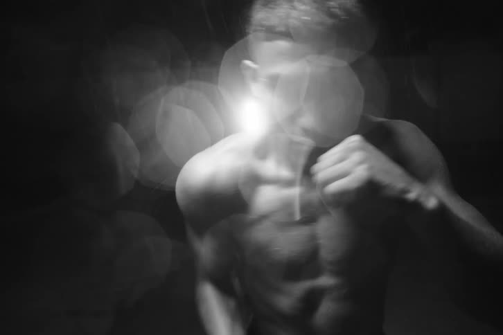 A shirtless young man boxing in front of the camera
