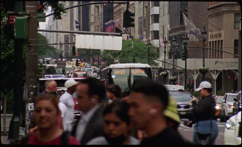Multiple cars and buses travel along a street that pedestrians are crossing
