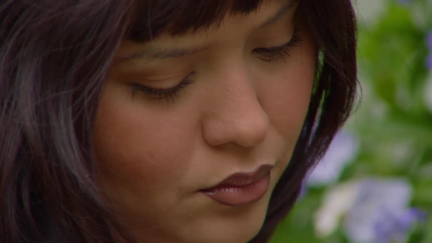 Woman with darkly outlined lips and dark hair in a garden with white and purple flowers