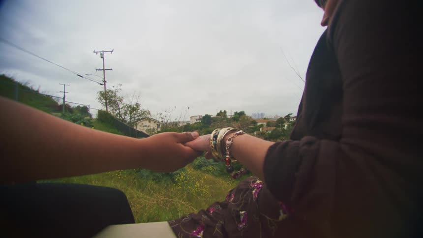 Young couple hold hands while sitting on a wall over a hill