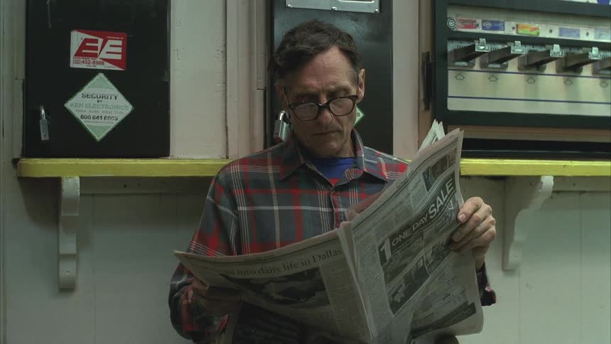 Older man sits and reads the newspaper near a coin operated machine