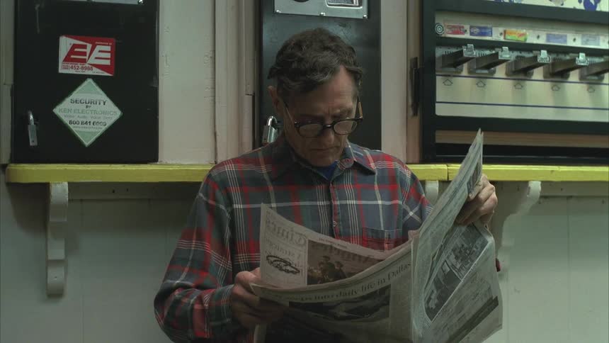 A man with glasses is reading a newspaper and changes the page