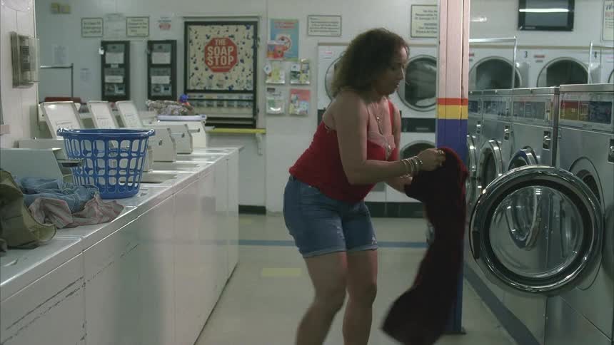Woman in a laundromat removing a red blanket from the washer and dryer