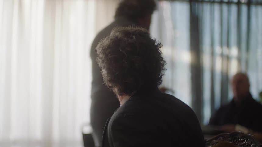 A person has his back turned you can see the back of his head and he is looking at a person who is walking behind him