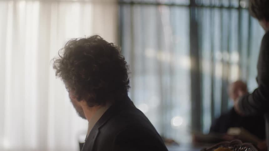 A man in a room listens as another man speaks