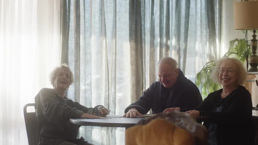 An elderly man and two women sit at a table laughing