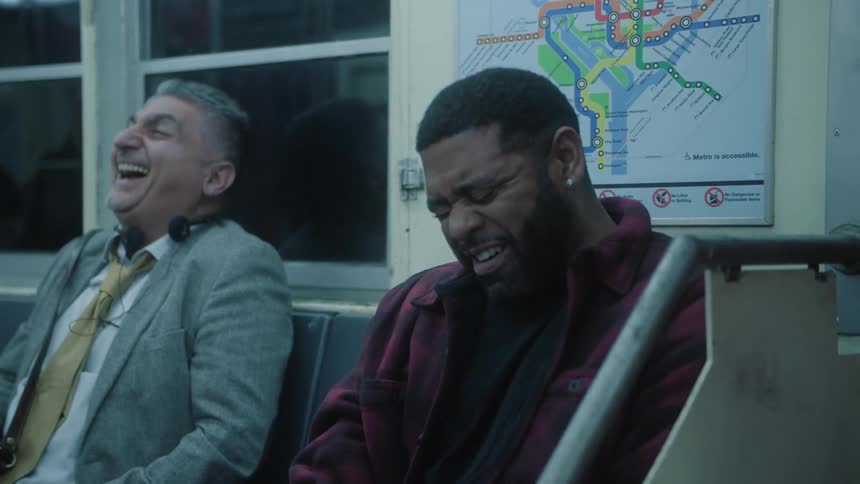 Two male passengers sitting on a train bench laughing