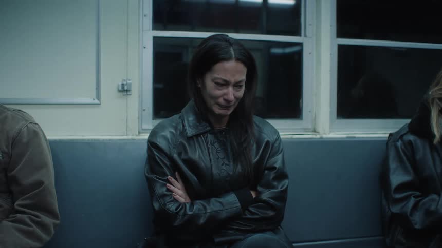 A woman sitting on a subway bench and she is starting to cry and puts her hand over her mouth