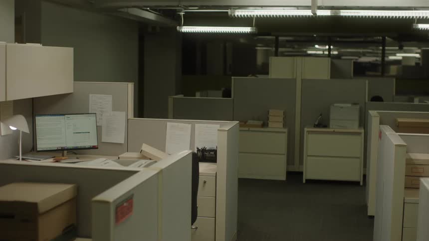 Bright office room with partitions and computers and in the background the silhouette of two people
