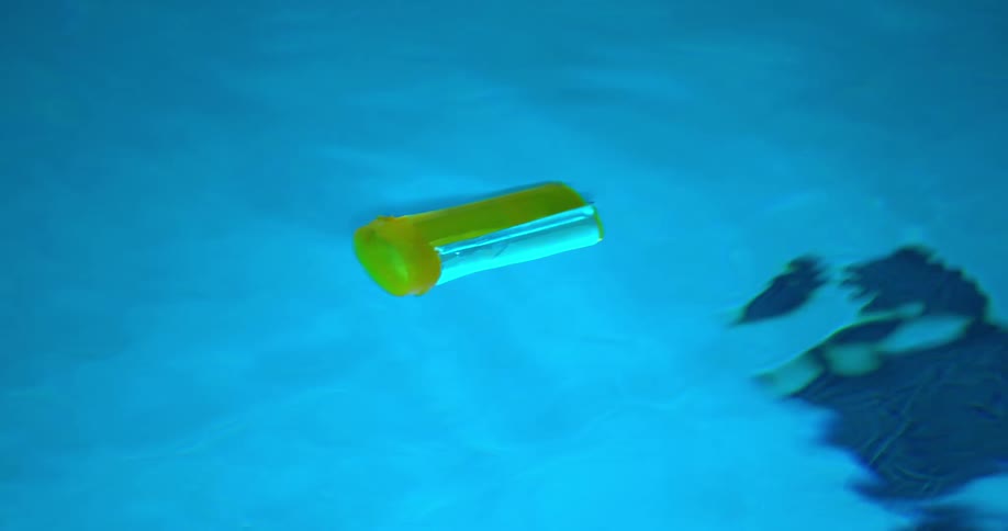 Closeup on a yellow medicine bottle floating in the water of a swimming pool