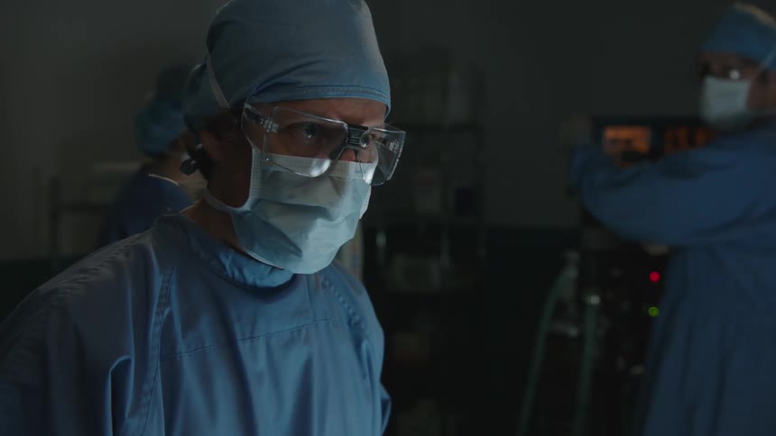 Doctors with glasses and protective mask inside a poorly lit surgical room