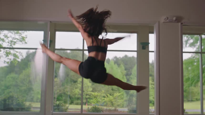 Back view of a female dancer doing a jump indoors and landing with her knees bent