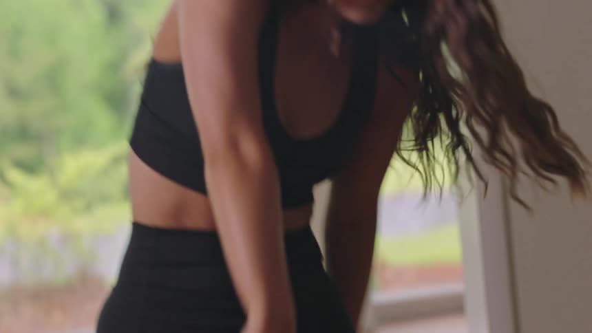 A young energetic woman wearing black sports clothes dances in a studio with large windows