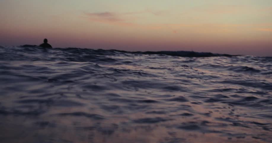 A surfer floating in the ocean at sunset