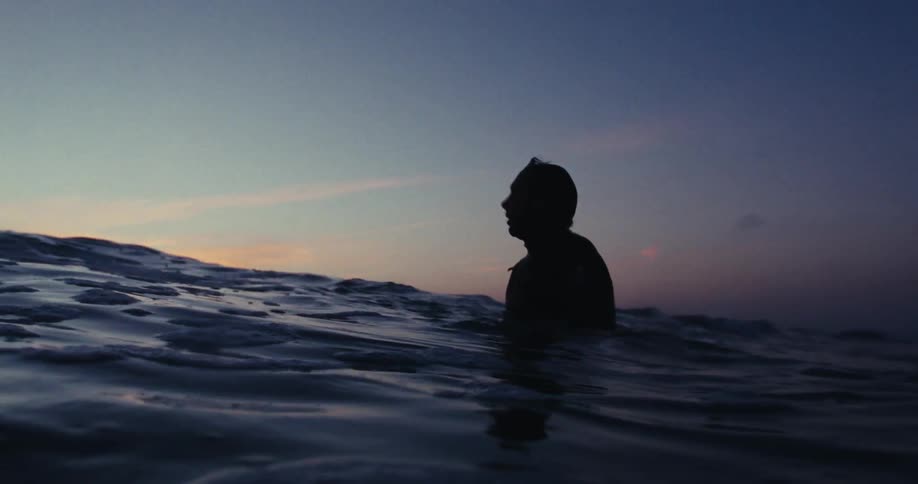 A man is standing in the shallow water at sunrise