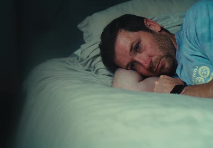 A sad looking man lying on a bed resting