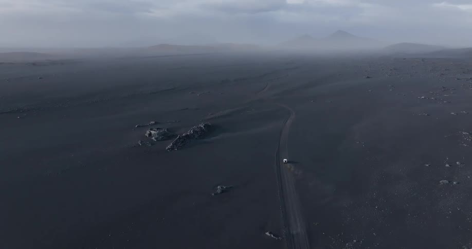 Aerial view of a lone car travels down a dirt road through a barren desert landscape