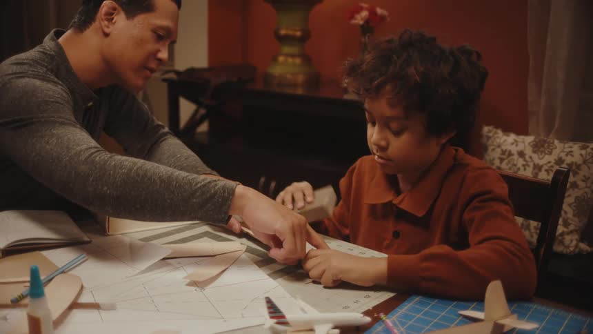 Father and son making toy paper planes in the living room