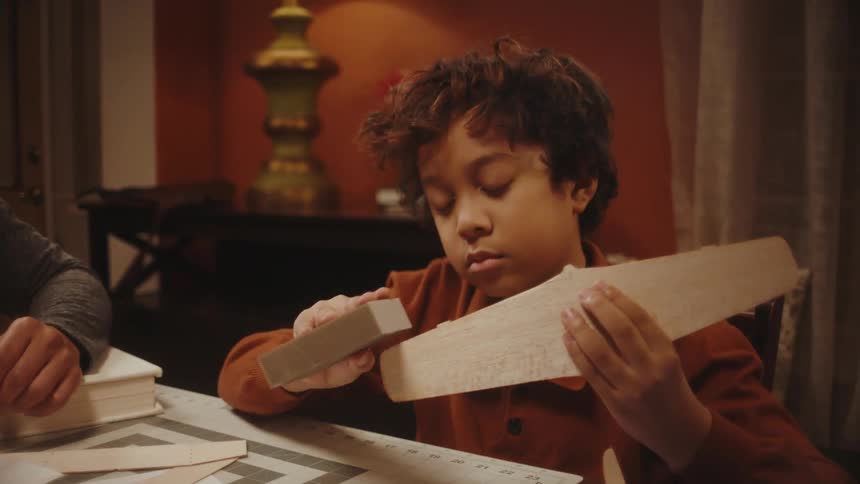 Father and son making toy paper planes in the living room