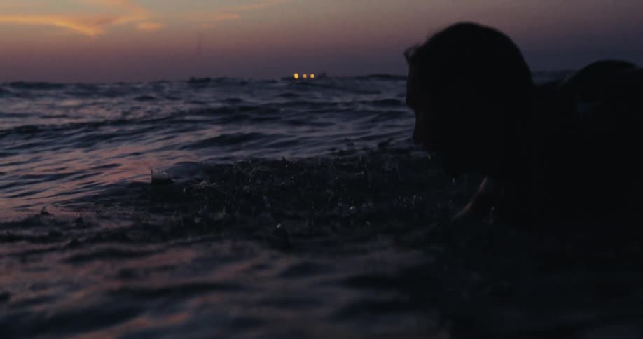A man swims on a surfboard in the ocean at dusk