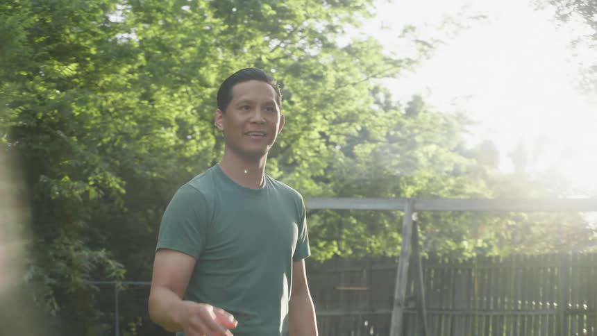 Man wearing a green t shirt and jeans plays with a jet paper airplane in the yard