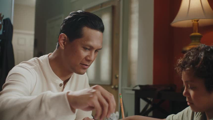 A father and son sit at a table and design a project with a ruler and paper