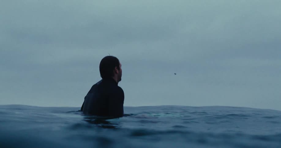 A man in a swimsuit stands in the sea by the beach on a cloudy day