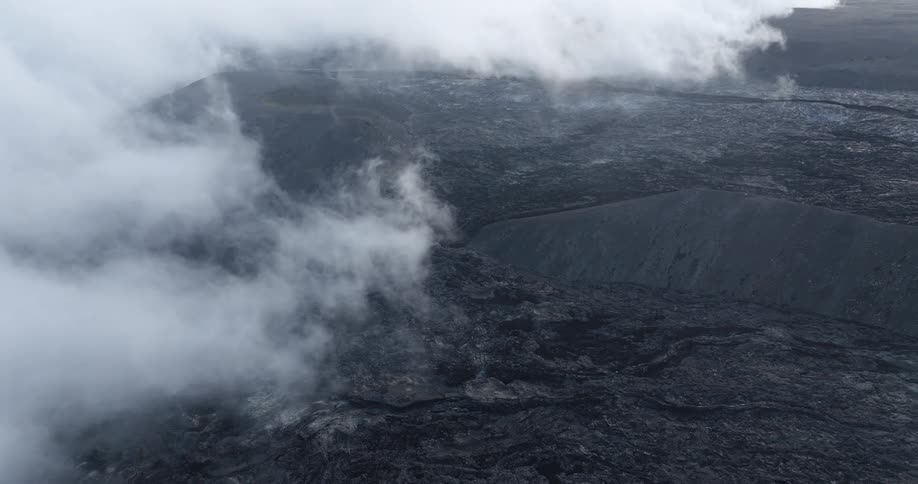 Aerial view of a dark volcanic landscape with smoke rising from the ground