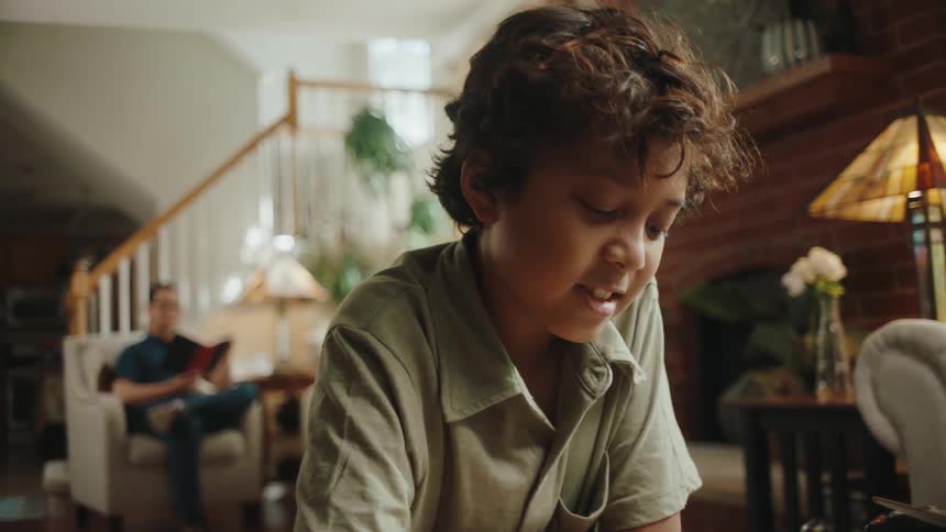 A man is sitting in an armchair and reading something and in front there is a little boy who is smiling while he sees something in front of him