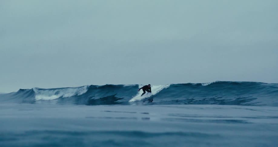 Man on a surfboard riding a wave under a cloudy sky