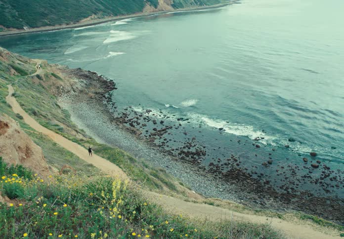 Aerial of a person walking on a dirt trail along the coast