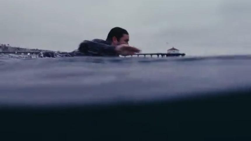 A surfer swimming over a surfboard on the ocean next to the docks