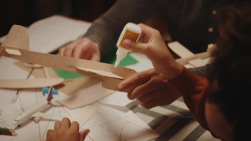 Father and son making toy paper planes in the living room