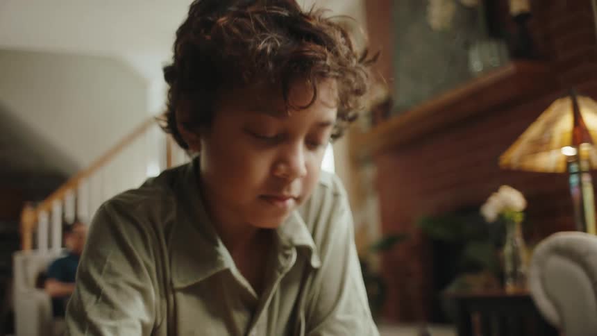Young boy doing homework on a coffee table in his living room
