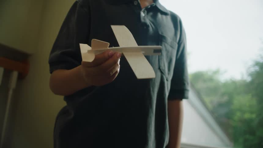 A boy with curly hair and a dark polo shirt plays with a small wooden airplane