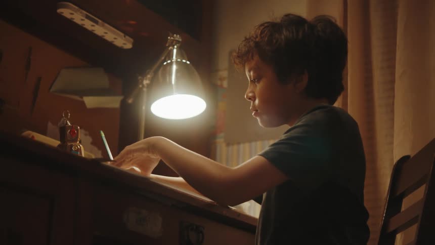 A young boy sits at a desk working on a project