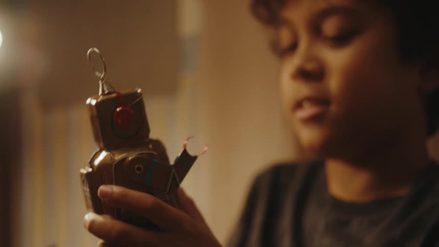 A boy playing with a small vintage toy robot at home