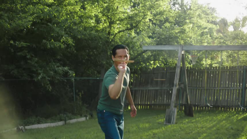 A man throws a toy plane in a backyard