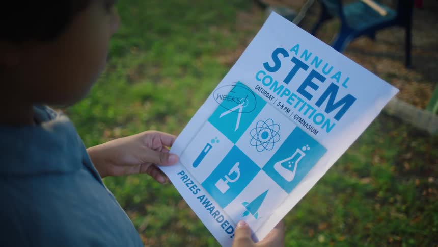 A boy holds a paper in his hand about a science competition