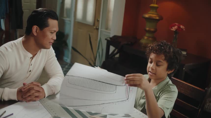 Father and son making toy paper planes in the living room