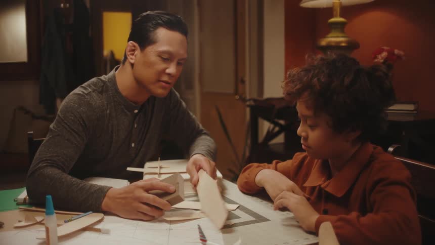 Father and son making toy paper planes in the living room