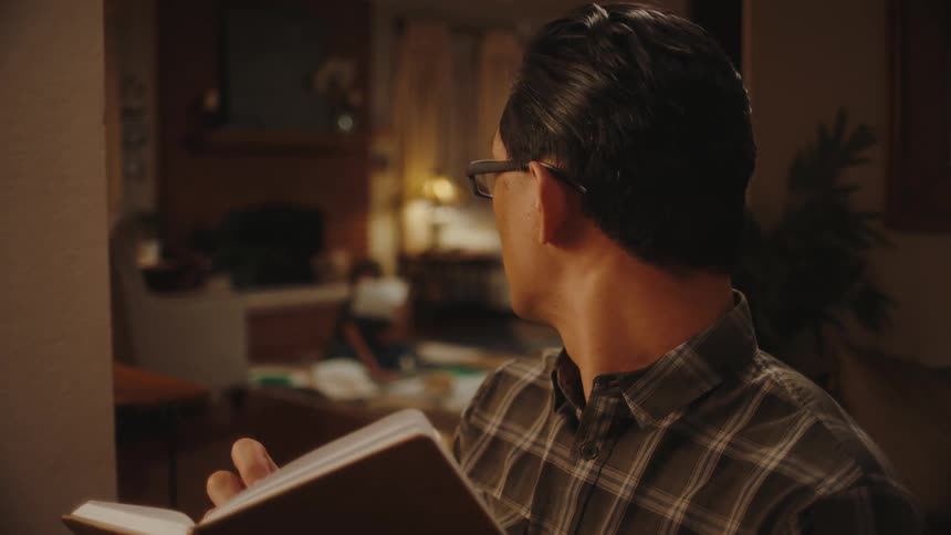 A man standing in the living room looks at his son while taking notes