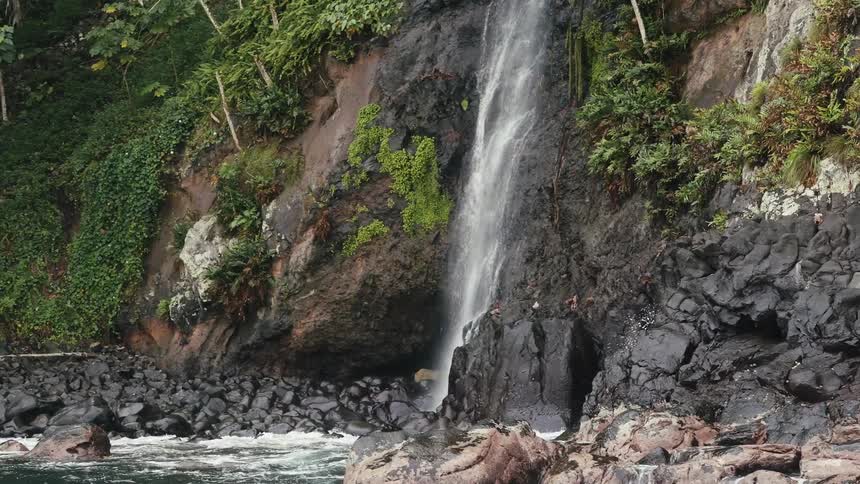 A small waterfall coming out of a stone mountain and falling onto the sea coast