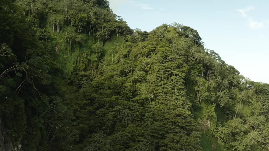 Two large hills covered with vegetation and forest and in the middle a waterfall