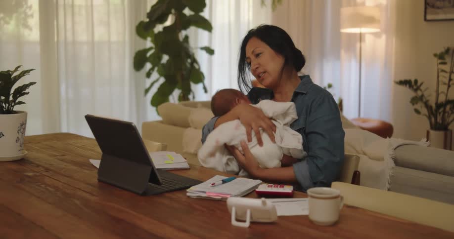 A mother rocks her baby while talking on the tablet