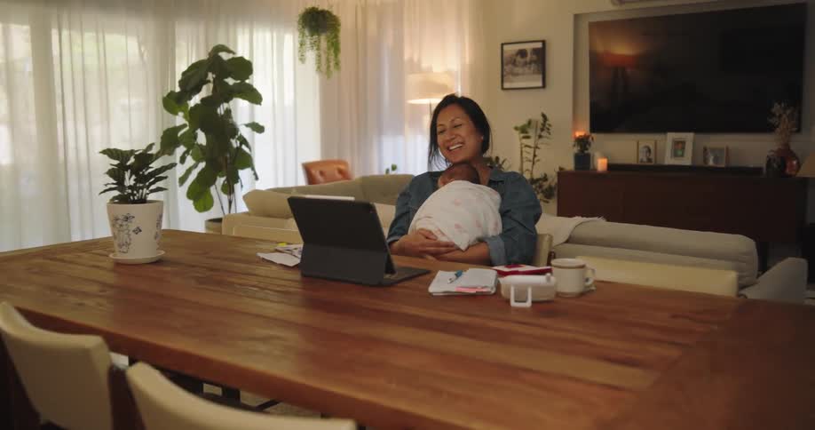 A woman is holding a baby while working on the computer